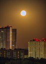 Deep night shot of a full moon over residential houses on the outskirts of a city. A bright moon disk illuminates high buildings Royalty Free Stock Photo