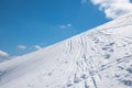 Deep powder snow piste with ski tracks, against blue sky
