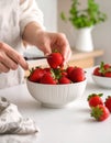 Deep red strawberries are being hulled with a small knife over a white ceramic bowl, for a dessert Royalty Free Stock Photo