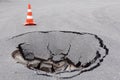 Deep sinkhole on street city and orange traffic cone. Dangerous hole in asphalt highway. Road with crack. Damaged surface collapse