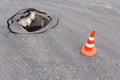 Deep sinkhole on street city and traffic cone. Dangerous hole in asphalt highway. Road with cracks. Bad construction. Damage