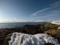 Deep snow on rocky sea shore with majestic blue sky, fjord and mountain background