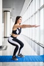 Deep squat. Side view of young beautiful woman in sportswear doing squat and holding dumbbells while standing in front Royalty Free Stock Photo