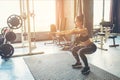 Deep squat of young beautiful woman in sportswear doing squat while standing in front of glass at gym