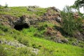 A deep stone cave and an entrance to it from the end of a low hill