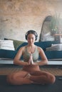 Deepen your practice with some calming sounds. a young woman meditating while practising yoga at home.