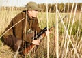 Deer hunting. A game hunter crouching down in the reeds in the outdoors with his rifle. Royalty Free Stock Photo