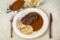 Deer meat, plum sauce and dumpling on plate, cutlery, sauce in bowl, wine in glass on table Royalty Free Stock Photo