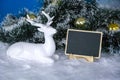 Deer in new year`s decor. A spruce branch with Golden Christmas balls and a sign for writing text. Design blank for greetings