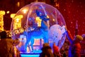 A deer standing in a large glass ball. People stand nearby and touch the outside. New year holiday