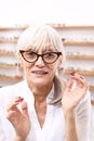Defect of vision. A senior woman in an optical salon chooses eyeglass frames.