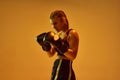 Defense position. Teen girl, concentrated MMA athlete in boxing gloves training against orange studio background in neon