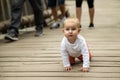 defenseless little blue-eyed white-haired child crawls on all fours on wooden flooring and is overtaken by adults.
