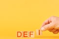 defi. man folds the inscription defi from wooden blocks on an orange background.