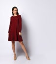 Gorgeous dark-haired young woman standing hands on hips in elegant dark-red sequin dress with long sleeves and nude stilettos Royalty Free Stock Photo