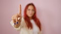 Defiant, young redhead woman asserts a bold \'no\', with a resolute hand gesture, over a pink isolated background Ã¢â¬â a