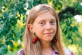 Defocus beautiful blond teen girl with sweet cherry on ear. Beautiful smiling teenage girl closeup, against green of Royalty Free Stock Photo