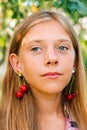 Defocus beautiful blond teen girl with sweet cherry on ear. Beautiful smiling teenage girl closeup on green of summer Royalty Free Stock Photo