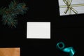 Defocus blank white card with fir tree branch, gift bow, craft envelope and blue ribbon on black background. Frame Royalty Free Stock Photo