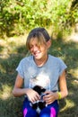 Defocus blonde little smiling girl playing with cat, black and white small kitten. Nature green summer background. Girl