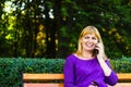 Defocus caucasian blond smiling woman talking, speaking on the phone outside, outdoor. 40s years old woman in purple Royalty Free Stock Photo