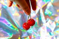 Defocus close-up hand holding two red wet sweet cherries with tail and leaves on modern hologram background. Fruits and Royalty Free Stock Photo