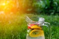 Defocus glass jug of lemonade with slice lemon and mint on natural green background with water drops. Pitcher of fresh