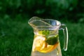 Defocus glass jug of lemonade with slice lemon and mint on natural green background with water drops. Pitcher of fresh