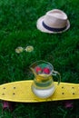 Defocus glass jug of lemonade with strawberry, slice lemon and leaves of mint on yellow board. Blurred grass background