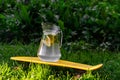 Defocus glass jug of lemonade with strawberry, slice lemon and leaves of mint on yellow penny board, skateboard. Blurred