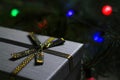 Defocus gray gift with close-up gold bow ribbon on pine or fir tree blurred background with glowing festive green and Royalty Free Stock Photo