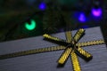 Defocus gray gift with close-up gold bow ribbon on pine or fir tree blurred background with glowing festive green and Royalty Free Stock Photo