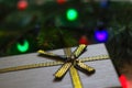 Defocus gray retro gift with close-up gold bow ribbon on pine or fir tree blurred background with glowing festive light Royalty Free Stock Photo