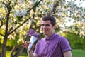 Defocus portrait of handsome smiling caucasian man with cone flowers in lilac garden. Funny young brunette guy smelling