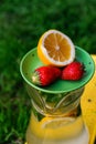 Defocus saucer with lemon and two strawberry standing on glass jug of lemonade with slice lemon and leaves of mint on Royalty Free Stock Photo