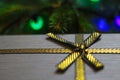Defocus side view gray retro gift with close-up gold bow ribbon on pine or fir tree blurred background with glowing Royalty Free Stock Photo