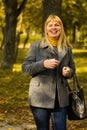 Defocus smiling blond 40s woman gesturing in yellow autumn park. Happy beautiful lady. Women wearing grey coat, pullover Royalty Free Stock Photo