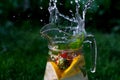 Defocus splash water bubbles in glass jug of lemonade with slice lemon, strawberry and mint on natural green background Royalty Free Stock Photo