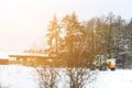 Defocus tractor clean snow sunny flare. Tractor cleaning snow in field. Big yellow tractor cleans up snow from the road Royalty Free Stock Photo