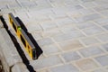 Defocus yellow spirit level on paving stone footpath. Monotone light gray brick stone pavement on the ground. Texture background. Royalty Free Stock Photo