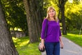 Defocus young blonde woman standing in park. Green nature background. Mature blonde woman smiling and looking at camera