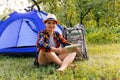 Defocus young woman working on tablet near camping tent outdoors surrounded by beautiful nature. Freelance, sabbatical