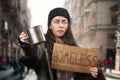 Defocused beggar woman holds a cardboard sign with the text homeless and steel alms cup. Defocused background with Royalty Free Stock Photo