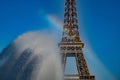 Rainbow on shiny fountain drops in front of Eiffel tower with clear blue sky background
