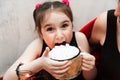 Defocused Funny little Girl Holding Cup with Hot Tasty Chocolate and Marshmellow and trying to eat it on cozy Red