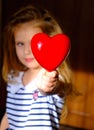 Defocused little girl with red heart at home, the rays of the morning sun illuminate dark room and heart.