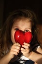 Defocused little girl with red heart at home, the rays of the morning sun soft illuminate dark room and heart. Real authentic life