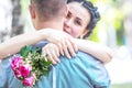 Defocused portrait of a beautiful young female bride with small wedding pink flower roses bouquet gently hugging bridegroom neck a Royalty Free Stock Photo