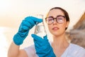 Defocused portrait of ecologist wearing protective gloves and eyeglasses, holds test sample flask of water. Concept of