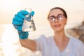 Defocused portrait of smiling ecologist wearing protective gloves and eyeglasses, holds test sample flask of pure water